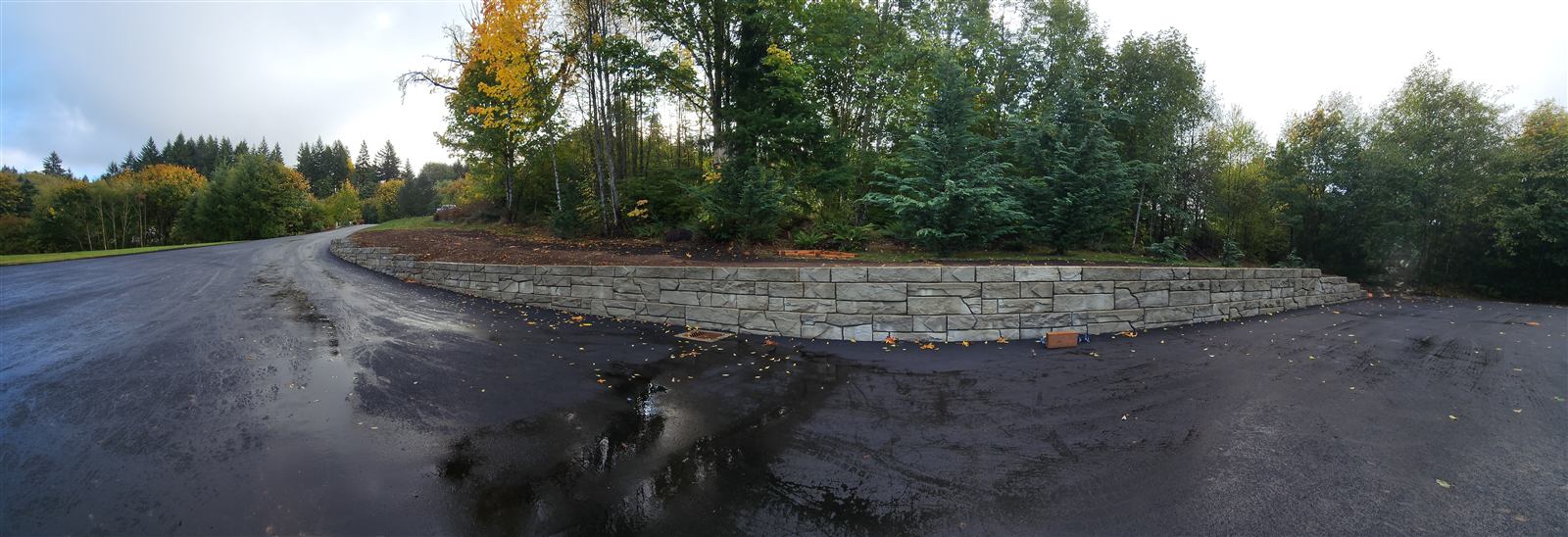 Curving Verti-Block wall along a wet road edge below trees